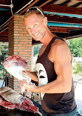Josh Galt III smiling, holding a leg of wild boar over a butchering table