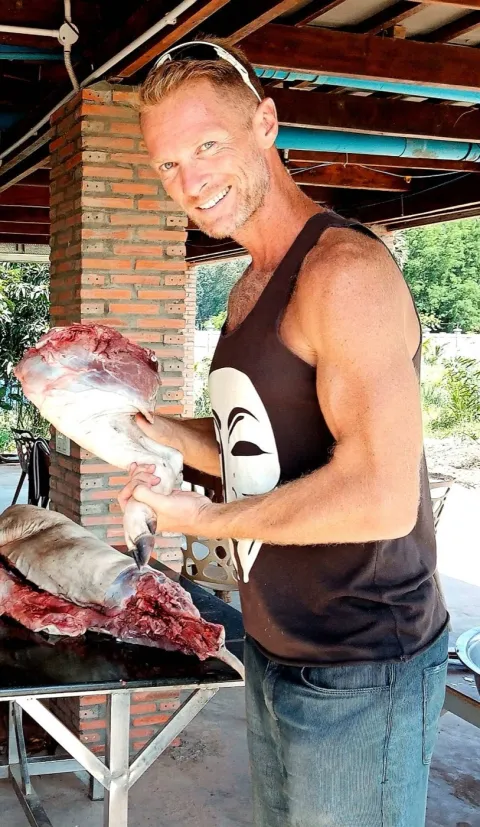 Josh Galt III smiling, holding a leg of wild boar over a butchering table